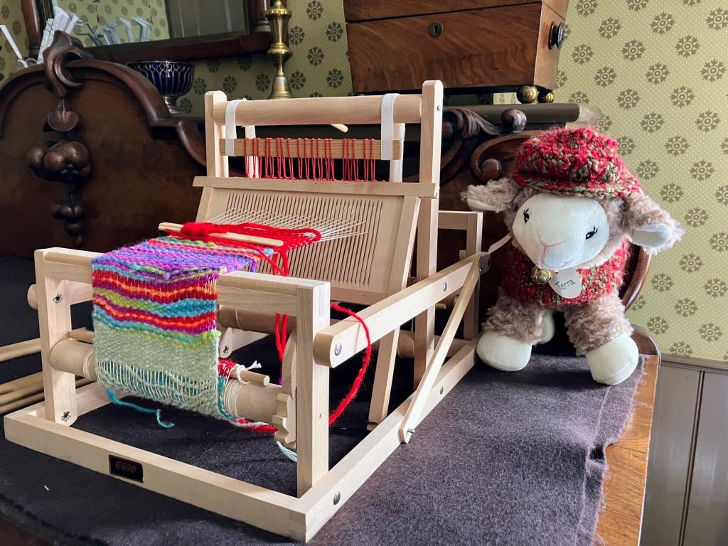 Small table loom with sheep Terra modeling hat knitted by the Gibson House Museum Youth Team.
