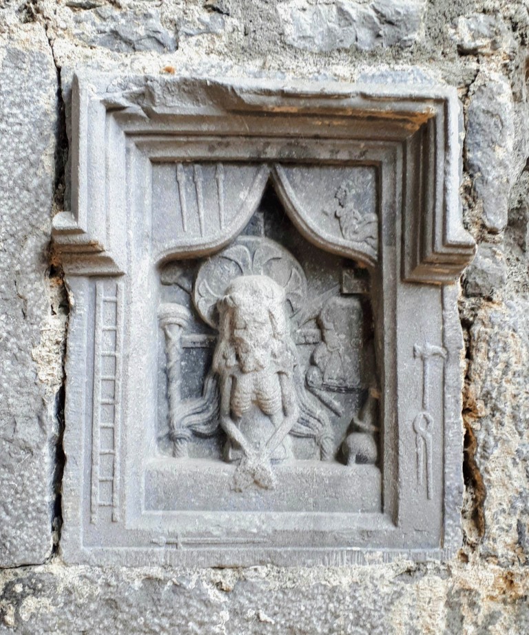 Carved image of Ecce Homo at Ennis Friary, showing Christ with bound hands, surrounded by tokens of the crucifixion (nails, hammer, spear, ladder, etc.).
