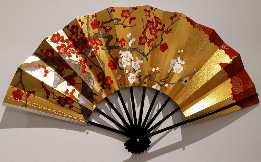 A Japanese dancing fan (Odori Mai Ogi) from the Fans Onstage exhibition for Nihon Buyō Dance and Kabuki. Gold and silver leaves on lacquered sticks, with white plum on golden background (front) and pine on silver background (back).